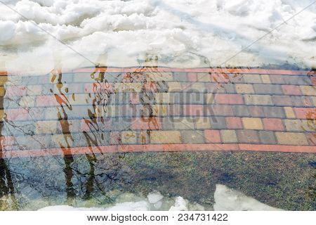 Flooding Of Tile Walkpath Due To Snow Melting And Rising Of Water Level. Blue Sky In Puddle Reflecti