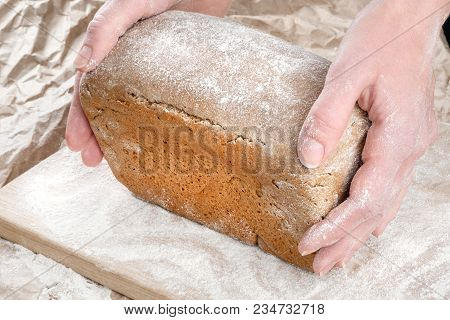 A Loaf Of Rye Gray Black Bread In Pink Hands Of A Woman On A Black Table Background. A Woman Holds B