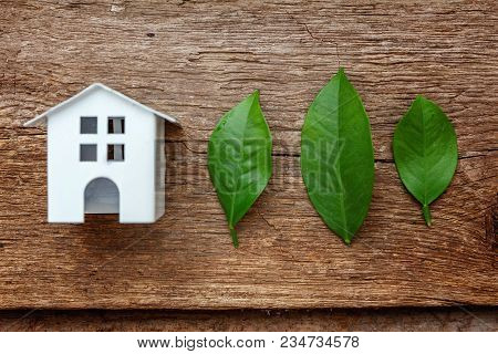 Miniature White Toy Model House With Green Leaves On Wooden Backgdrop. Eco Village, Abstract Environ