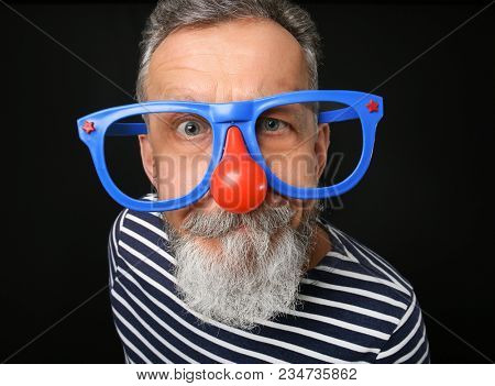 Mature man in funny disguise on dark background. April fool's day celebration