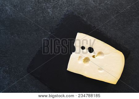 An Appetizing Solid Cheese On A Black Plate On A Gray Stone Background