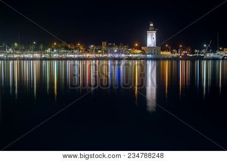 View Of Malaga City And Lighthouse And Their Reflections On Water From Harbour, Malaga, Spain
