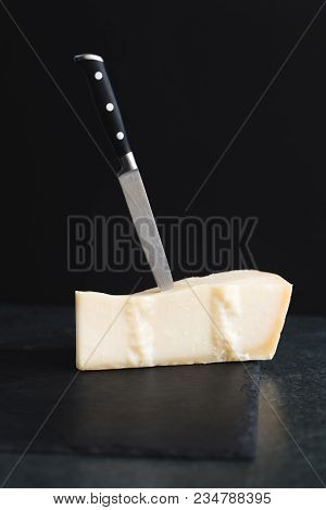 An Appetizing Solid Cheese On A Black Plate On A Gray Stone Background