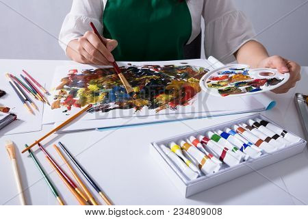 Artist Holding Paint Palette While Painting On Canvas Paper