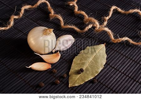 Onion, Garlic, Black Pepper And Bay Leaf On A Black Table
