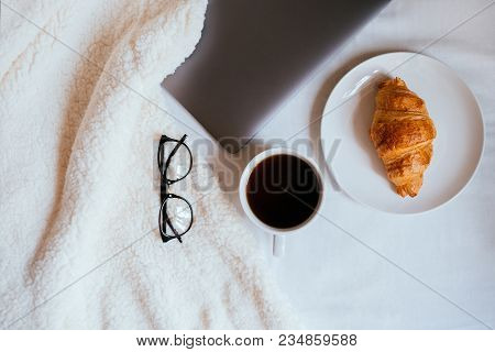 Big White Morning Cup Of Coffee And Crossant In Bed With Notebook, Glasses, Pillow And Cosy Blanket.
