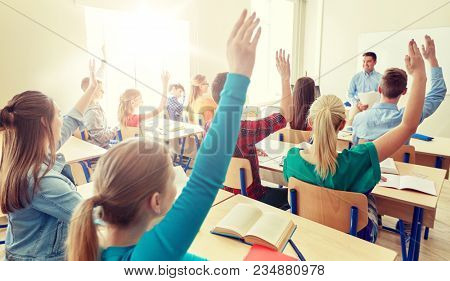 education, high school, teaching, learning and people concept - group of happy students raising hands and teacher in classroom