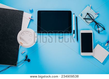 Workspace Of A Creative Student. Studying With A Cup Of Coffee, Using Phone And Tablet On Blue Backg