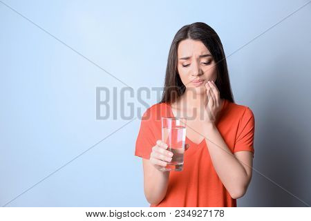 Woman With Sensitive Teeth Holding Glass Of Water On Color Background