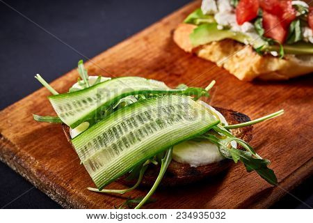 Grilled Toast Brisket With Tomato, Avocado And Ruccola On Wooden Cutting Board Over Dark Background,