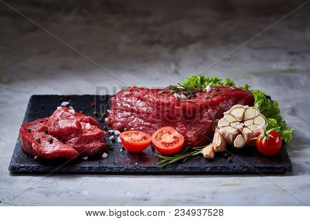 Yummy Composition Of Raw Beefsteak On Slate Board With Rosemary, Spicies, Garlic, Tomatoes, Letucce 