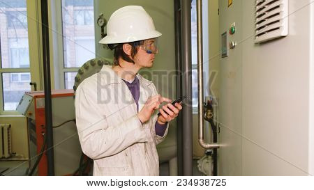 The Engineer In A White Helmet And Goggles Writes Data To The Smartphone From The Display Of The Ele