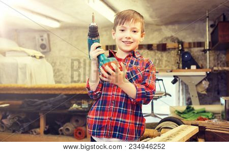 children, carpentry, profession and people concept - happy little boy with drill at workshop