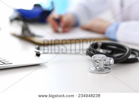 Closeup Of Stethoscope. Female Doctor Fills Up Medical Form While Sitting At The Desk In Hospital. H