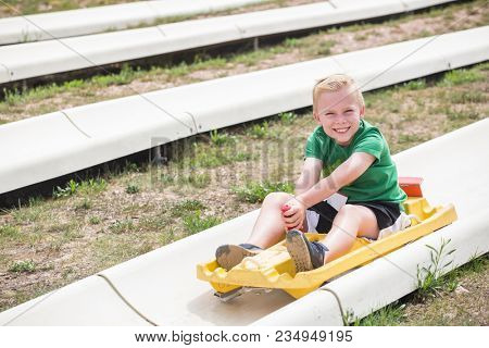 Cute smiling young boy riding downhill on an alpine coaster ride outdoors on a summers day. Happy and having fun on a thrilling theme park ride