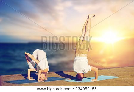 fitness, people and healthy lifestyle concept - couple doing yoga headstand outdoors on wooden pier over sea background