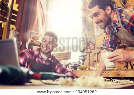 profession, carpentry, technology, woodwork and people concept - two carpenters with laptop computer at workshop