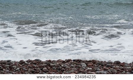 The Beach With Colorful Pebbles And A Bustling Ocean. Background