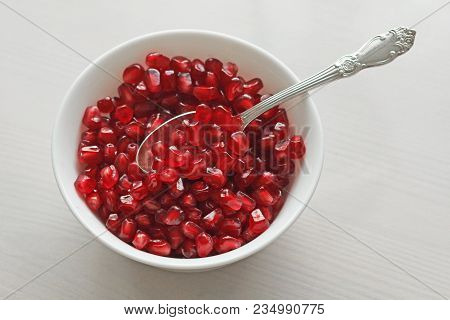 Grains Of Red Ripe Pomegranate Lie In A White Bowl With A Spoon. Big Ripe Red Granets Or Garnets. Fr