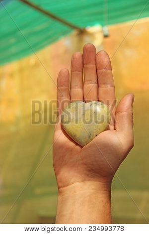 The Hand Holds A Heart Made Of Natural Stone Yellow Jadeite. Heart In Hand. A Stone In The Shape Of 