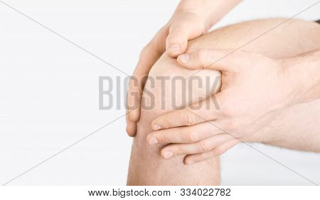 A Man In Underwear Holds His Knee With A Hand On A Gray Background.
