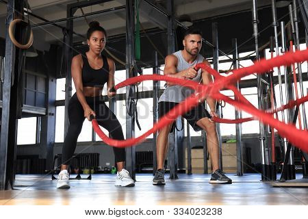 Athletic Young Couple With Battle Rope Doing Exercise In Functional Training Fitness Gym.