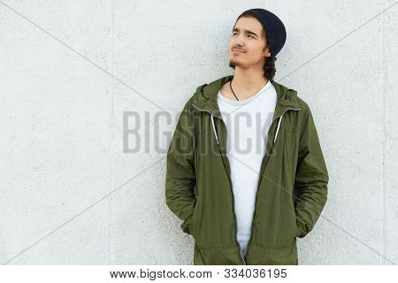 Thoughtful Dreaming Mysterious Young Man With Curly Hair Wearing White T Shirt, Black Trendy Hat And