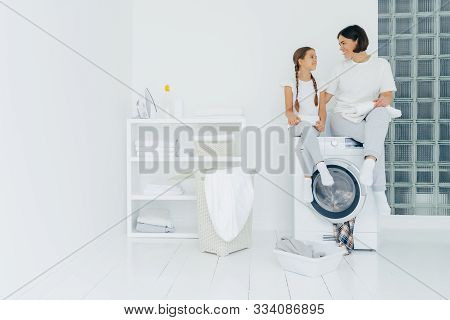 Housewife And Small Child Sit On Top Of Washing Machine, Holds Freshly Washed Towels, Do Washing Tog
