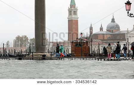 People On The Walkway In Venice Island In Italy During The Tide And The Church Of Saint George In Ba