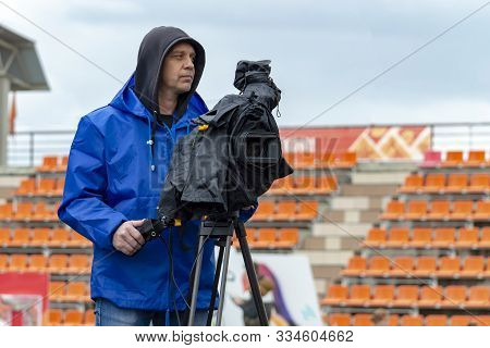 Man With Video Camera. In Rain, Camera Is Covered With Waterproof Black Cover. Holiday - Oilman Day,