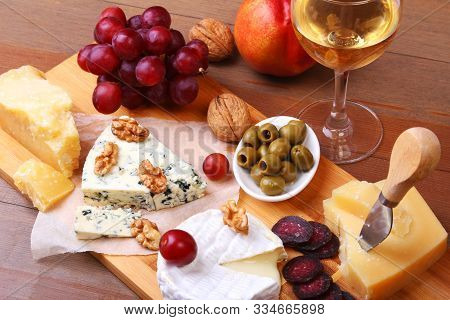 Assortment Of Cheese With Fruits, Grapes, Nuts And Cheese Knife On A Wooden Serving Tray.