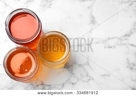 Jars With Different Types Of Organic Honey On White Marble Table, Flat Lay. Space For Text