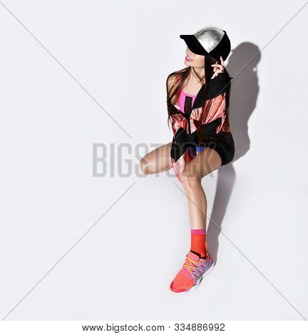 Stylish Athletic Girl In A Long Bomber And Cap, Posing While Sitting On A Light Background In The St