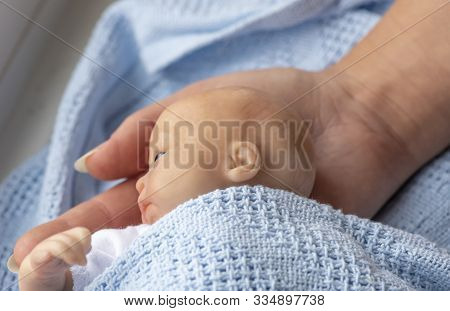 Premature Newborn Baby Wrapped In Blue Blanket With Mothers  Arm And Hand Represented By A Reborn Do