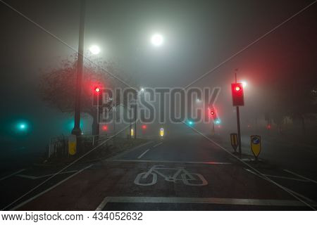 Colored Traffic Lights And White Street Lights Shine Through Thick Night Time Fog At A Road Junction