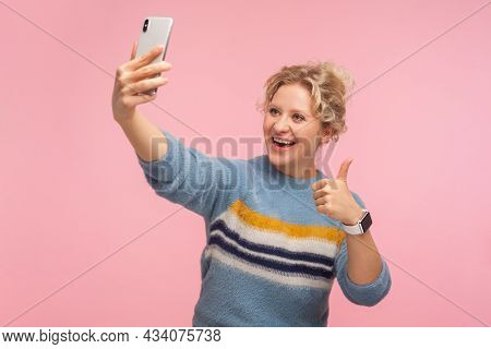 Portrait Of Excited Pretty Woman With Curly Hair In Sweater Showing Thumbs Up Gesture And Taking Sel