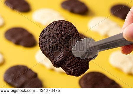 Hand Pcking Up Chocolate Mexican Skull With Tongs On Yellow Background