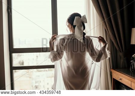 The Brunette Takes Off Her White Robe In A Hotel Room Against The Background Of The Window. Young Se