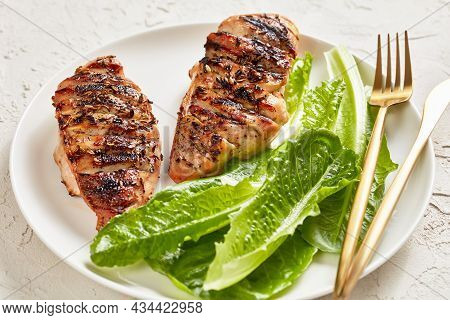 Seared Chicken Breasts With Fresh Romaine Lettuce Leaves On A White Plate With Golden Cutlery On A W