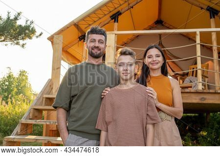 Happy parents and their teenage son standing by glamping house in natural environment