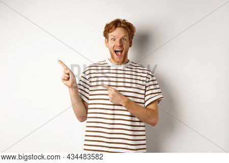 Cheerful Man With Red Hair Checking Out Promo Offfer, Pointing Left At Logo And Smiling At Camera, S