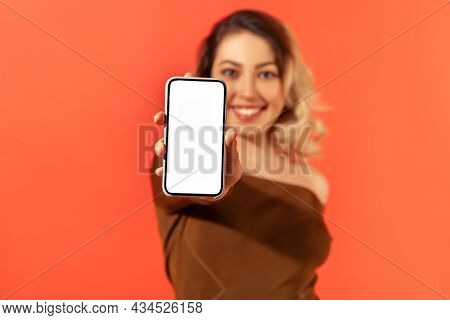Positive Smiling Woman Holding And Showing Smartphone With Empty White Display, Freespace For Your A