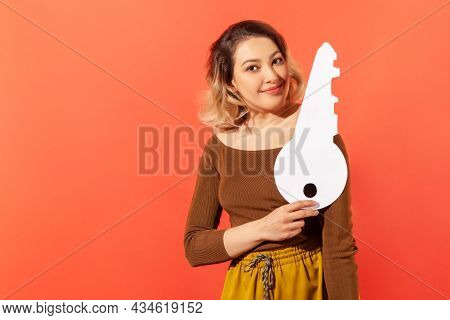 Smiling Happy Woman Holding In Hand Big Paper Key As Symbol Of Her Own Apartment, Dreams Comes True,