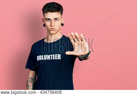 Young caucasian boy with ears dilation wearing volunteer t shirt doing stop sing with palm of the hand. warning expression with negative and serious gesture on the face. 