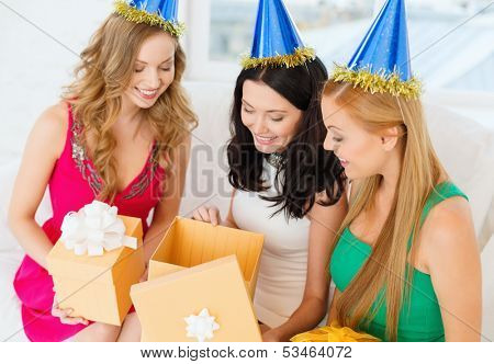 celebration, friends, bachelorette party, birthday concept - three smiling women wearing blue hats with gift boxes