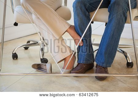 Casual businesswoman playing footsie with colleague under desk in the office