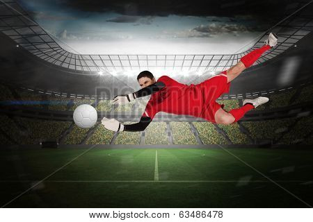 Fit goal keeper jumping up in a large football stadium with lights