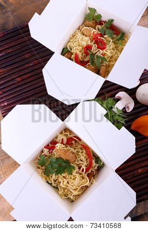 Chinese noodles in takeaway boxes on bamboo mat background