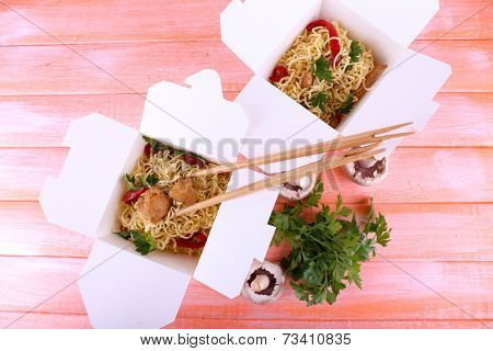 Chinese noodles with meat and pepper in takeaway boxes on pink background