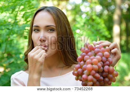 Beautiful slender girl eating healthy fruit. Portrait of pretty young woman holding ripe grapes bunch